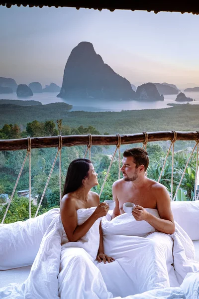 Couple waking up in bed in nature jungle looking out over ocean during sunrise at wooden hut in the moutains of Thailand — Stok fotoğraf