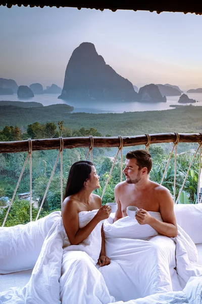Couple waking up in bed in nature jungle looking out over ocean during sunrise at wooden hut in the moutains of Thailand — 图库照片