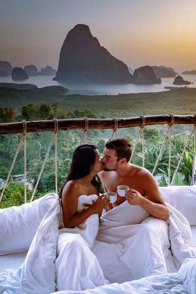 Couple waking up in bed in nature jungle looking out over ocean during sunrise at wooden hut in the moutains of Thailand — Stok fotoğraf