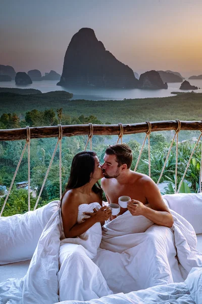 Couple waking up in bed in nature jungle looking out over ocean during sunrise at wooden hut in the moutains of Thailand — Stockfoto