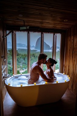 couple watching sunset in bathtub in the bathroom during vacation in Thailand watching sunset over the ocean and moutnains 