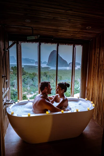 Couple watching sunset in bathtub in the bathroom during vacation in Thailand watching sunset over the ocean and moutnains — Stok fotoğraf