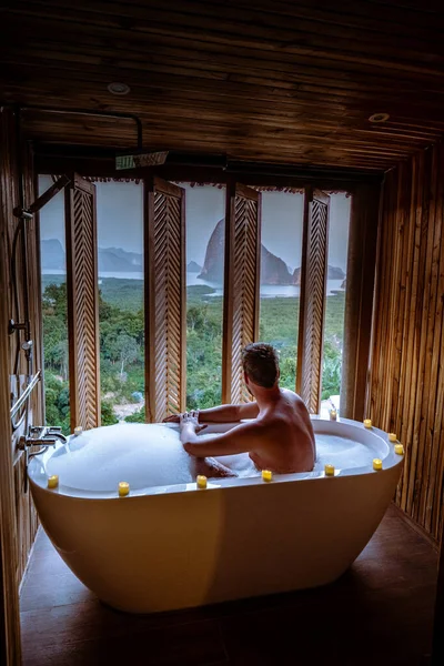 Men watching sunset in bathtub in the bathroom during vacation in Thailand watching sunset over the ocean and moutnains — Stok fotoğraf