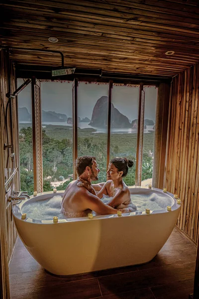 Couple watching sunset in bathtub in the bathroom during vacation in Thailand watching sunset over the ocean and moutnains — Stok fotoğraf