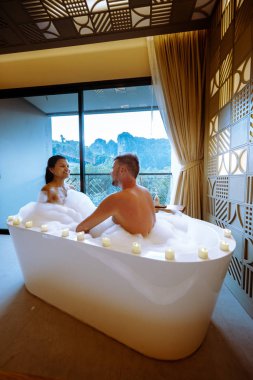Couple in bath watching sunset in bathtub in the bathroom during vacation in Thailand watching sunset over the ocean and moutnains 