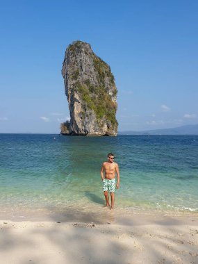 Guy in swim short on the beach of Koh poda Island Krabi Thailand, men in yellow short on the beach on a bright sunny day with blue sky