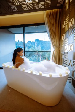 woman in bath watching sunset in bathtub in the bathroom during vacation in Thailand watching sunset over the ocean and moutnains 