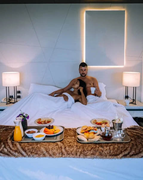 couple having breakfast in bed, men and woman in luxury room and white bed having breakfast in bed