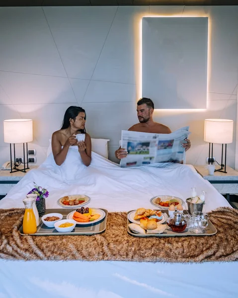 Couple prenant le petit déjeuner au lit, hommes et femmes dans une chambre de luxe et lit blanc prenant le petit déjeuner au lit — Photo