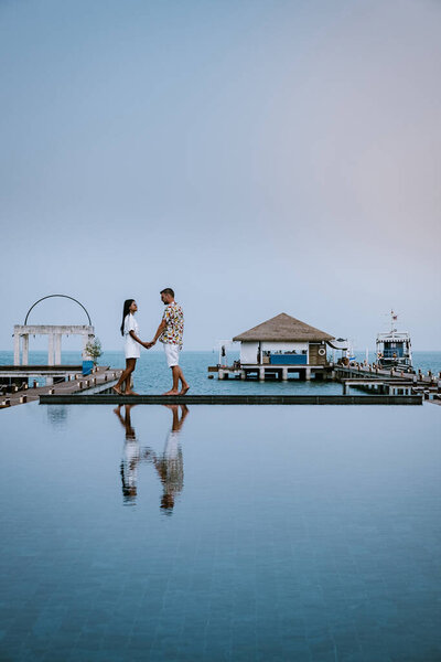 couple on a luxury vacation in thailand walking by the ocean with pool and bleu sky 