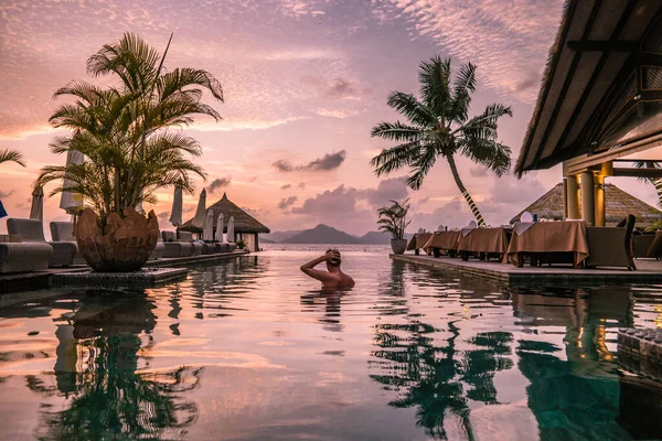 Luxury swimming pool in tropical resort, relaxing holidays in Seychelles islands. La Digue, Young man during sunset by swimpool — Zdjęcie stockowe