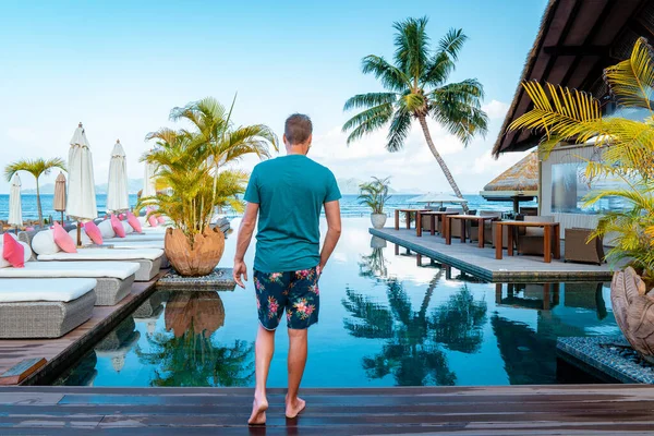 Luxury swimming pool in tropical resort, relaxing holidays in Seychelles islands. La Digue, Young man during sunset by swimpool — Stockfoto