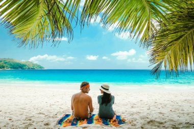 Praslin Adası 'ndaki tropikal beyaz plaj Seyşeller, tatilde genç bir çift, tatilde bir palmiye ağacının altında dinleniyor.