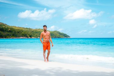 Praslin Seyşeller, tropikal sahilde palmiye ağacıyla gezen genç erkekler, Seyşeller Adası 'nda yürüyen beyaz plaj adamı, tropik tatilde bronzlaşan adamlar.