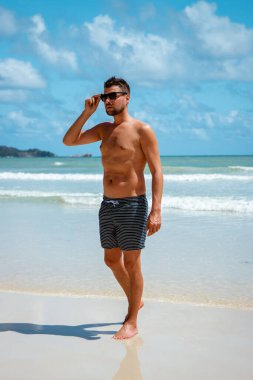 Praslin Seyşeller, tropikal sahilde palmiye ağacıyla gezen genç erkekler, Seyşeller Adası 'nda yürüyen beyaz plaj adamı, tropik tatilde bronzlaşan adamlar.