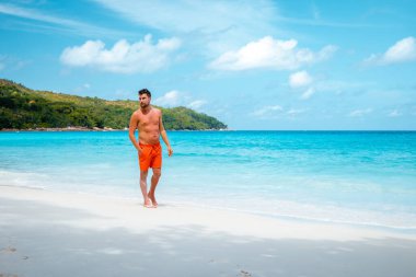 Praslin Seyşeller, tropikal sahilde palmiye ağacıyla gezen genç erkekler, Seyşeller Adası 'nda yürüyen beyaz plaj adamı, tropik tatilde bronzlaşan adamlar.