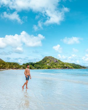 Praslin Seyşeller, tropikal sahilde palmiye ağacıyla gezen genç erkekler, Seyşeller Adası 'nda yürüyen beyaz plaj adamı, tropik tatilde bronzlaşan adamlar.