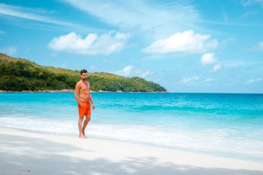 Praslin Seyşeller, tropikal sahilde palmiye ağacıyla gezen genç erkekler, Seyşeller Adası 'nda yürüyen beyaz plaj adamı, tropik tatilde bronzlaşan adamlar.