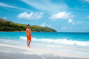 Praslin Seyşeller, tropikal sahilde palmiye ağacıyla gezen genç erkekler, Seyşeller Adası 'nda yürüyen beyaz plaj adamı, tropik tatilde bronzlaşan adamlar.