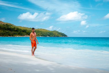 Praslin Seyşeller, tropikal sahilde palmiye ağacıyla gezen genç erkekler, Seyşeller Adası 'nda yürüyen beyaz plaj adamı, tropik tatilde bronzlaşan adamlar.