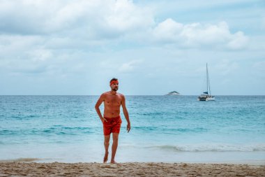 Praslin Seyşeller, tropikal sahilde palmiye ağacıyla gezen genç erkekler, Seyşeller Adası 'nda yürüyen beyaz plaj adamı, tropik tatilde bronzlaşan adamlar.