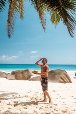 Praslin Seyşeller, tropikal sahilde palmiye ağacıyla gezen genç erkekler, Seyşeller Adası 'nda yürüyen beyaz plaj adamı, tropik tatilde bronzlaşan adamlar.