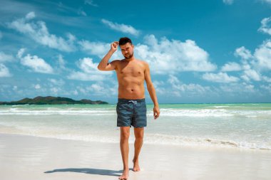 Praslin Seyşeller, tropikal sahilde palmiye ağacıyla gezen genç erkekler, Seyşeller Adası 'nda yürüyen beyaz plaj adamı, tropik tatilde bronzlaşan adamlar.