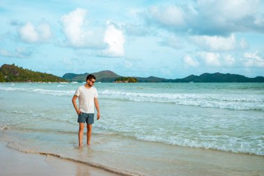 Praslin Seyşeller, tropikal sahilde palmiye ağacıyla gezen genç erkekler, Seyşeller Adası 'nda yürüyen beyaz plaj adamı, tropik tatilde bronzlaşan adamlar.