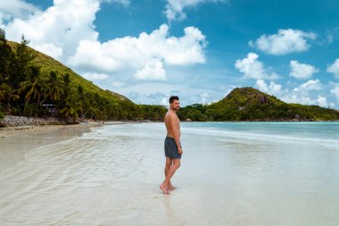 Praslin Seyşeller, tropikal sahilde palmiye ağacıyla gezen genç erkekler, Seyşeller Adası 'nda yürüyen beyaz plaj adamı, tropik tatilde bronzlaşan adamlar.