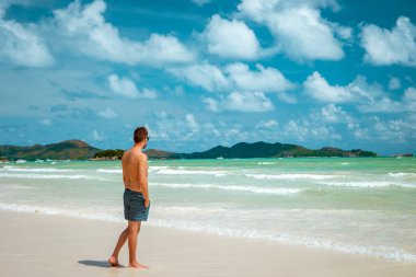 Praslin Seyşeller, tropikal sahilde palmiye ağacıyla gezen genç erkekler, Seyşeller Adası 'nda yürüyen beyaz plaj adamı, tropik tatilde bronzlaşan adamlar.