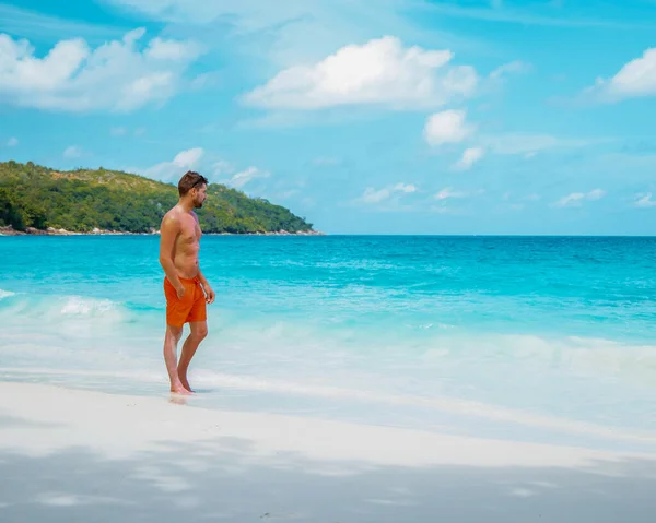 Praslin Seychely, mladí muži na tropické pláži s palmami, bílý plážový muž na procházce Seychely Island, opalování muži na tropické dovolené — Stock fotografie