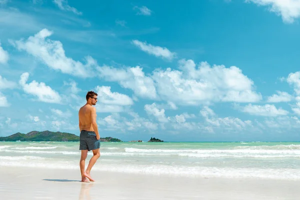 Praslin Seyşeller, tropikal sahilde palmiye ağacıyla gezen genç erkekler, Seyşeller Adası 'nda yürüyen beyaz plaj adamı, tropik tatilde bronzlaşan adamlar. — Stok fotoğraf