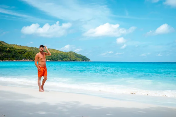 Praslin Seychellerna, unga män på tropisk strand med palm, vit strandman promenader Seychellerna Island, garvning män på tropisk semester — Stockfoto
