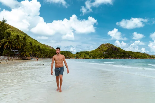 Praslin Seyşeller, tropikal sahilde palmiye ağacıyla gezen genç erkekler, Seyşeller Adası 'nda yürüyen beyaz plaj adamı, tropik tatilde bronzlaşan adamlar. — Stok fotoğraf