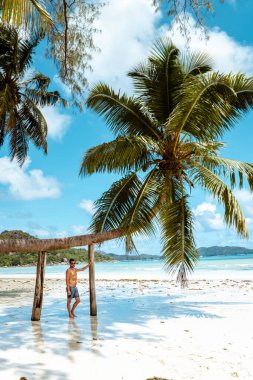 Praslin Seyşeller, tropikal sahilde palmiye ağacıyla gezen genç erkekler, Seyşeller Adası 'nda yürüyen beyaz plaj adamı, tropik tatilde bronzlaşan adamlar.