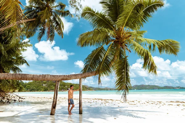 Praslin Seychellen, jonge mannen op tropisch strand met palmboom, witte strandman wandelend op het eiland Seychellen, bruinende mannen op tropische vakantie — Stockfoto