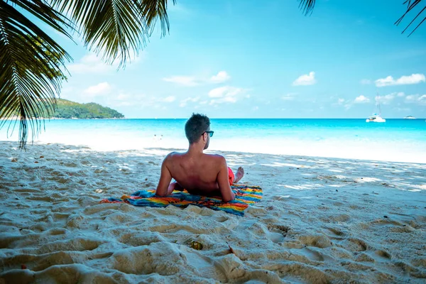 Praslin Seychellen, junge Männer am tropischen Strand mit Palme, weißer Strandmann auf den Seychellen, Sonnenanbeter im Tropenurlaub — Stockfoto