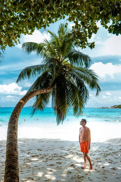 塞舌尔的祈祷者、热带海滩上手握棕榈树的年轻人、在塞舌尔岛上散步的白人、正在热带度假的晒太阳的男人 — 图库照片