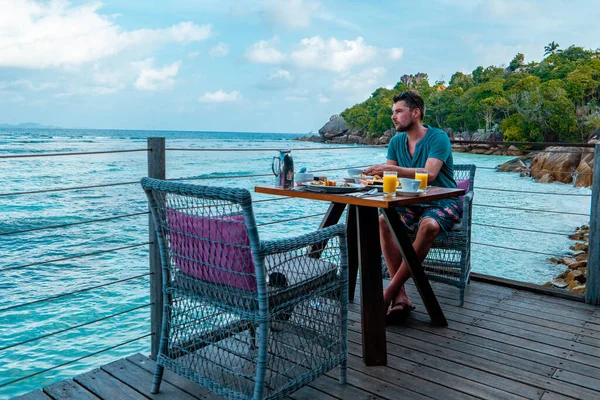 Mannen ontbijten aan de kust Seychellen, mannen oceanfrant zitten aan tafel brekafast Seychellen eten — Stockfoto
