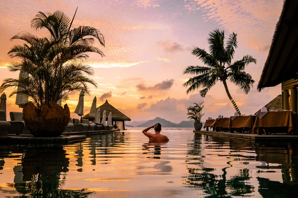 Luxury swimming pool in tropical resort, relaxing holidays in Seychelles islands. La Digue, Young man during sunset by swimpool — Stockfoto