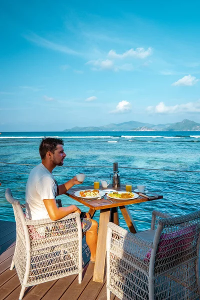 Hommes prenant le petit déjeuner front de mer Seychelles, hommes océanfrant assis à la table manger brekafast Seychellen — Photo