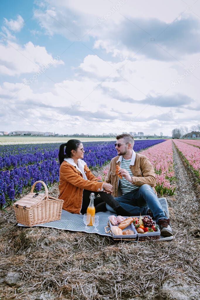 Spring flower season in the Netherlands, couple having a picnic during sprin in the bulb region by Lisse with Hyacinth flowers field on the background