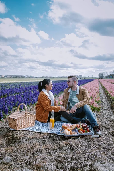 Lente bloemenseizoen in Nederland, koppel picknicken tijdens de lente in de bollenstreek van Lisse met Hyacint bloemenveld op de achtergrond — Stockfoto