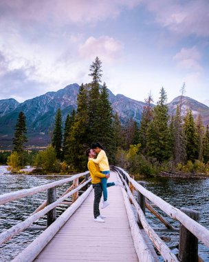 Çiftler göl kenarında gün batımını izliyor, Alberta Kanada 'da sonbahar boyunca Jasper Piramidi, günbatımında göl kenarına düşen renkler, Jasper Piramidi.