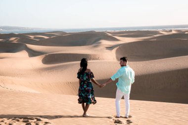 Maspalomas sahilinde yürüyen çift Gran Canaria İspanya, Maspalomas 'ın kum tepeleri çölünde kadın ve erkek.