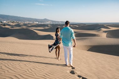Maspalomas sahilinde yürüyen çift Gran Canaria İspanya, Maspalomas 'ın kum tepeleri çölünde kadın ve erkek.