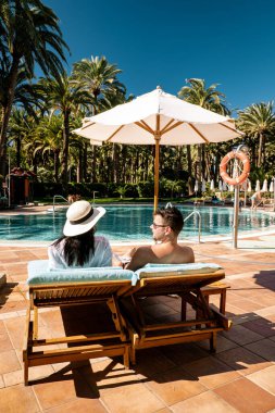 Yüzme havuzunda yataklı sandalyeler, lüks tatil köyü, plaj sandalyesinde dinlenen birkaç erkek ve kadın.