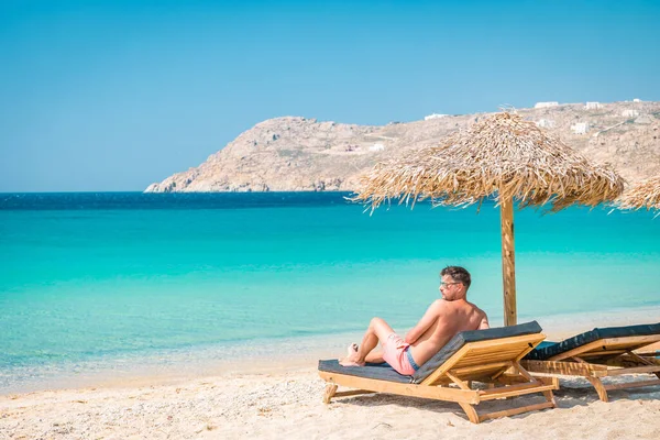 여름에는 우산 과 고급 비치 의자가 있는 해변 의자가 있는 미코노스 해변, 엘리아 해변 미코노스 그리스에 산 이 있는 푸른 바다 — 스톡 사진