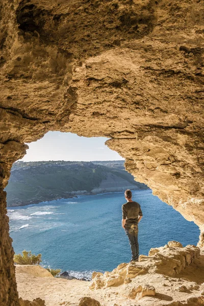 Isla de Gozo Malta, joven en una cueva con vistas al océano y a la bahía de Ramla, desde el interior de la cueva de Tal Mixta Gozo — Foto de Stock