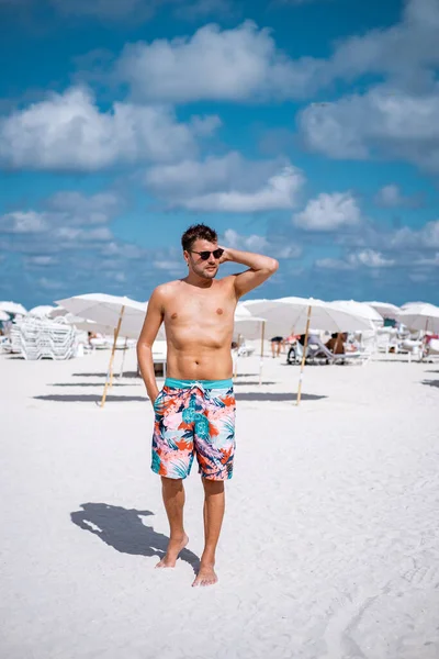 Miami Beach Florida, hombres jóvenes en la playa con cabaña de salvavidas colorido, hombre caminando en la playa en Miami durante las vacaciones — Foto de Stock